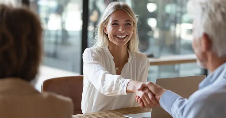 Lächelnde Frau schüttelt Hände mit älterem Mann im Büro